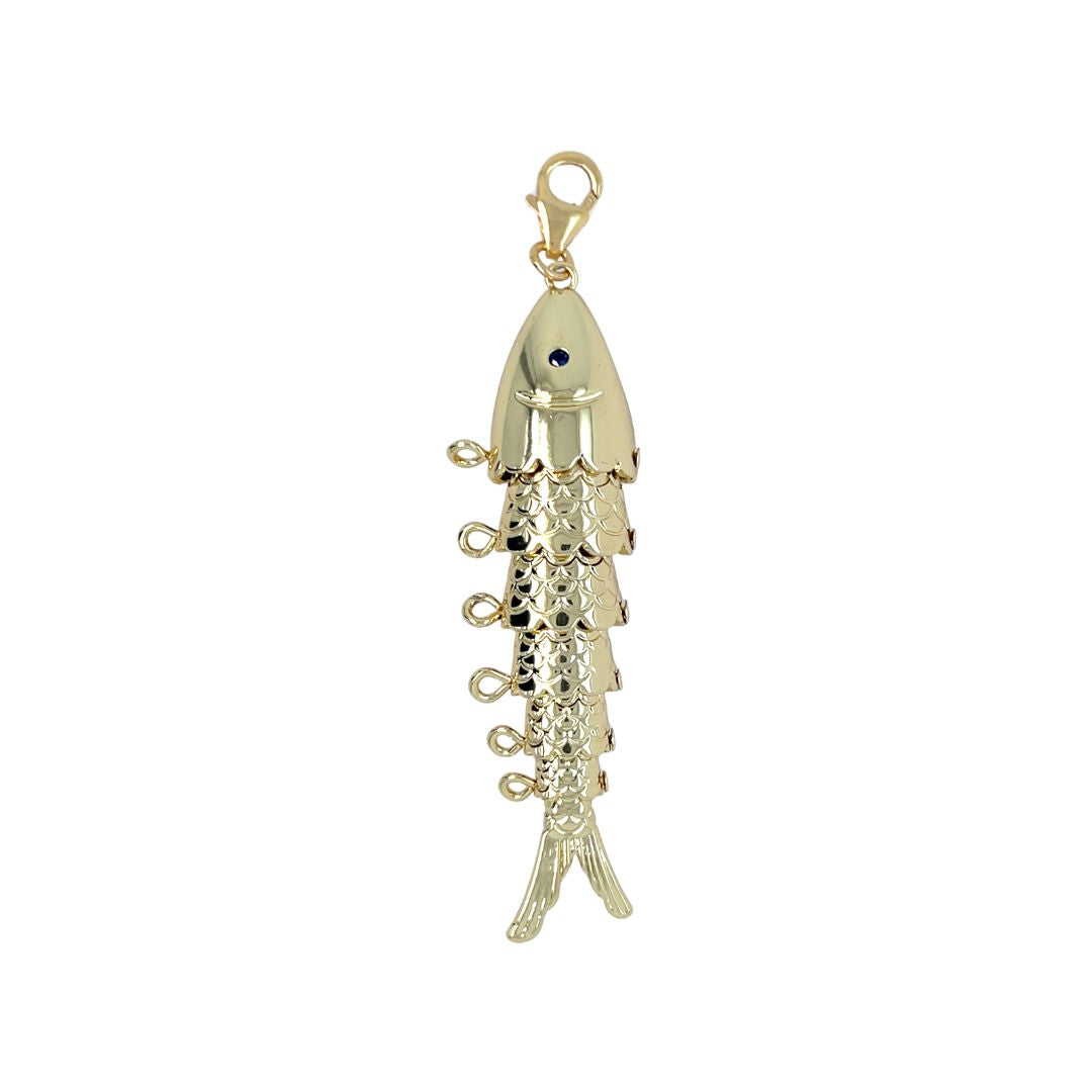 A gold fish-shaped charm pendant with a textured scale pattern, a small dark blue eye, and a lobster clasp at the top, shown on a plain white background.