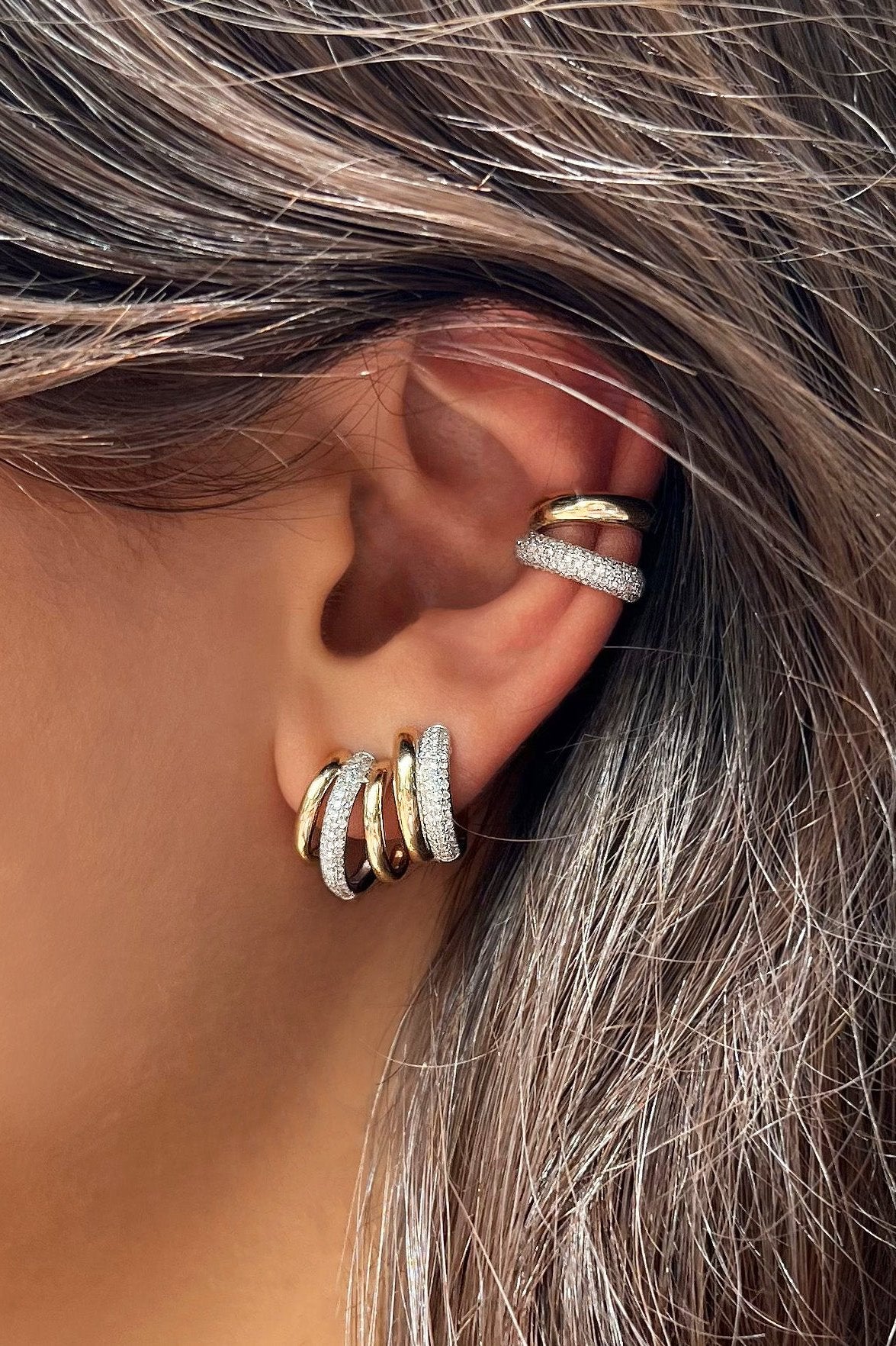 Close-up of a woman wearing earrings with a multi diamond and gold hoop earrings and ear cuffs.