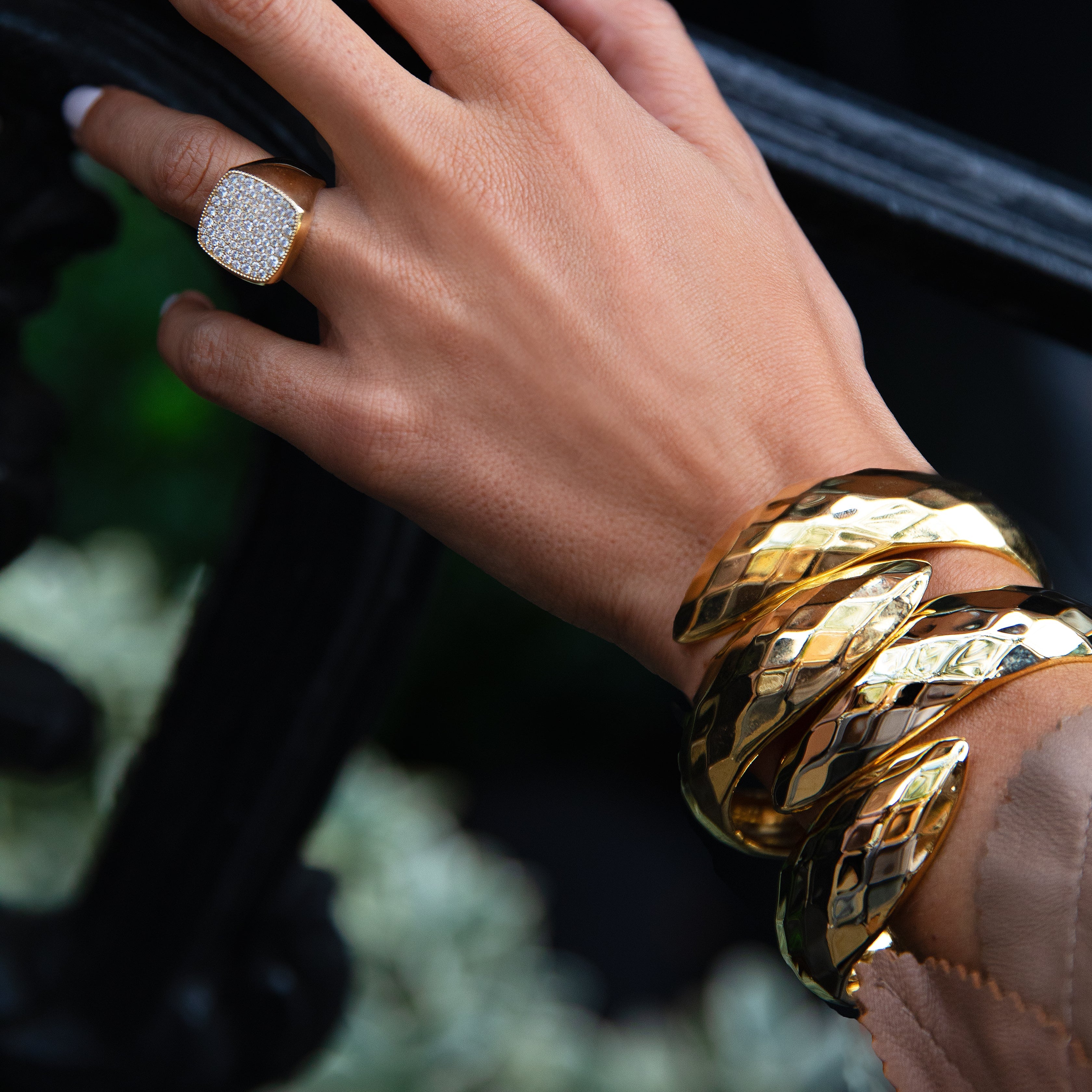 Hand wearing gold bracelets and ring on a blurred background