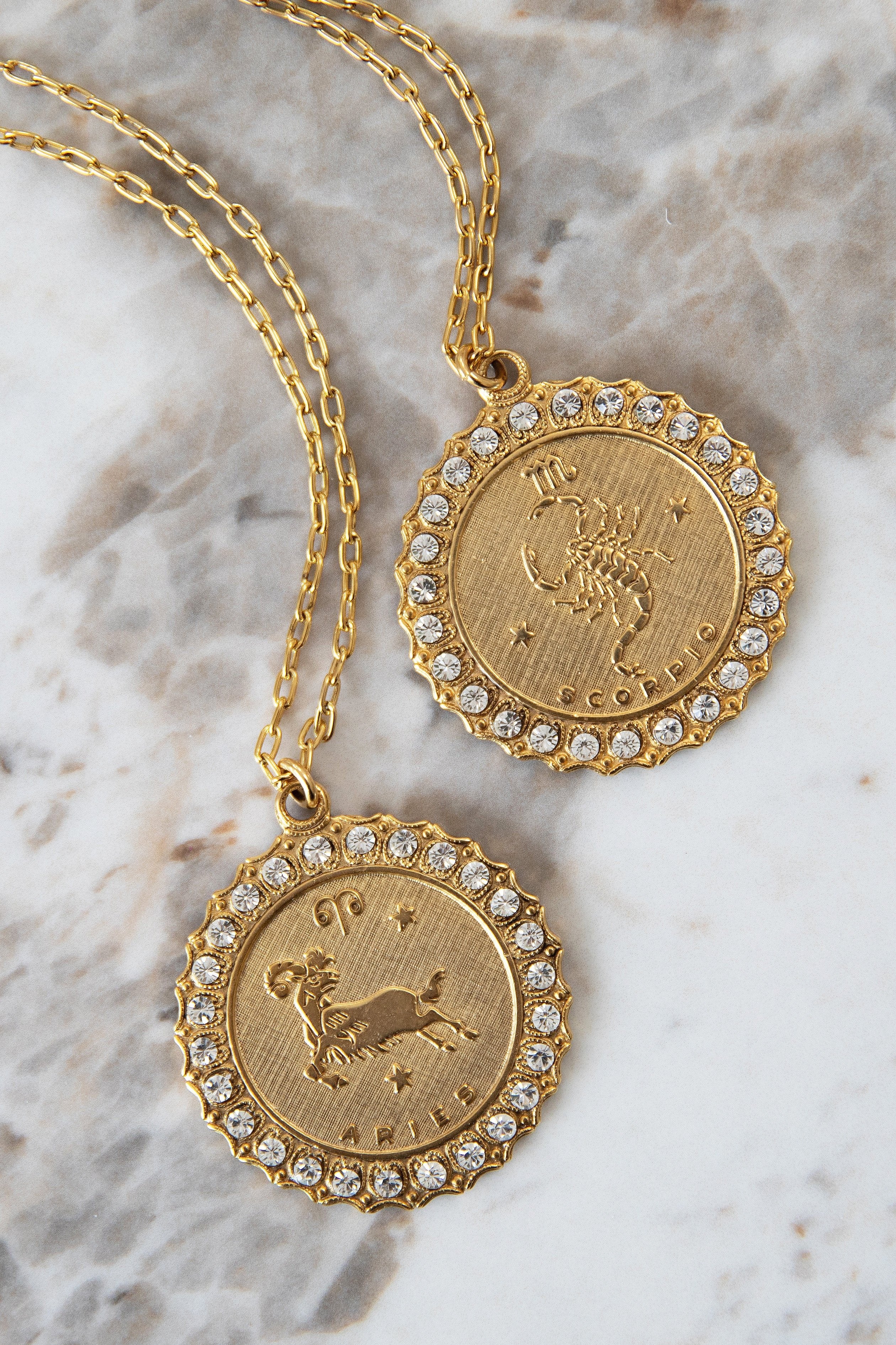Aries and Scorpio horoscope necklace on a marble background.