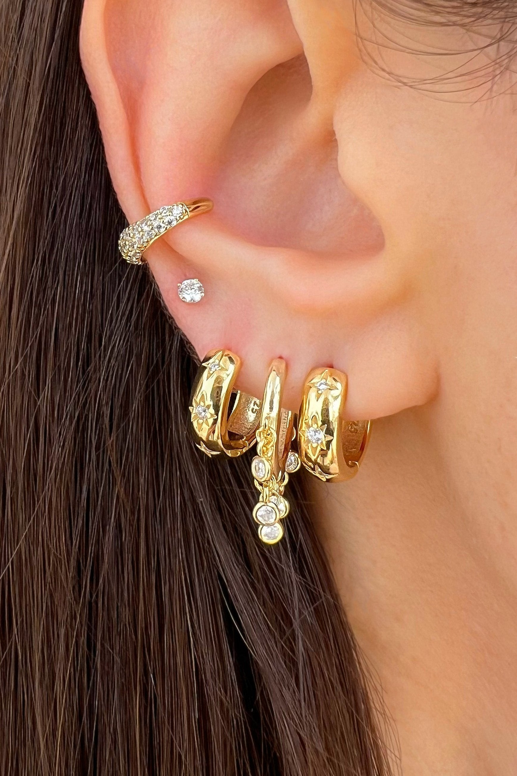 An ear decorated with multiple gold huggies, cz ear cuff, and studs.
