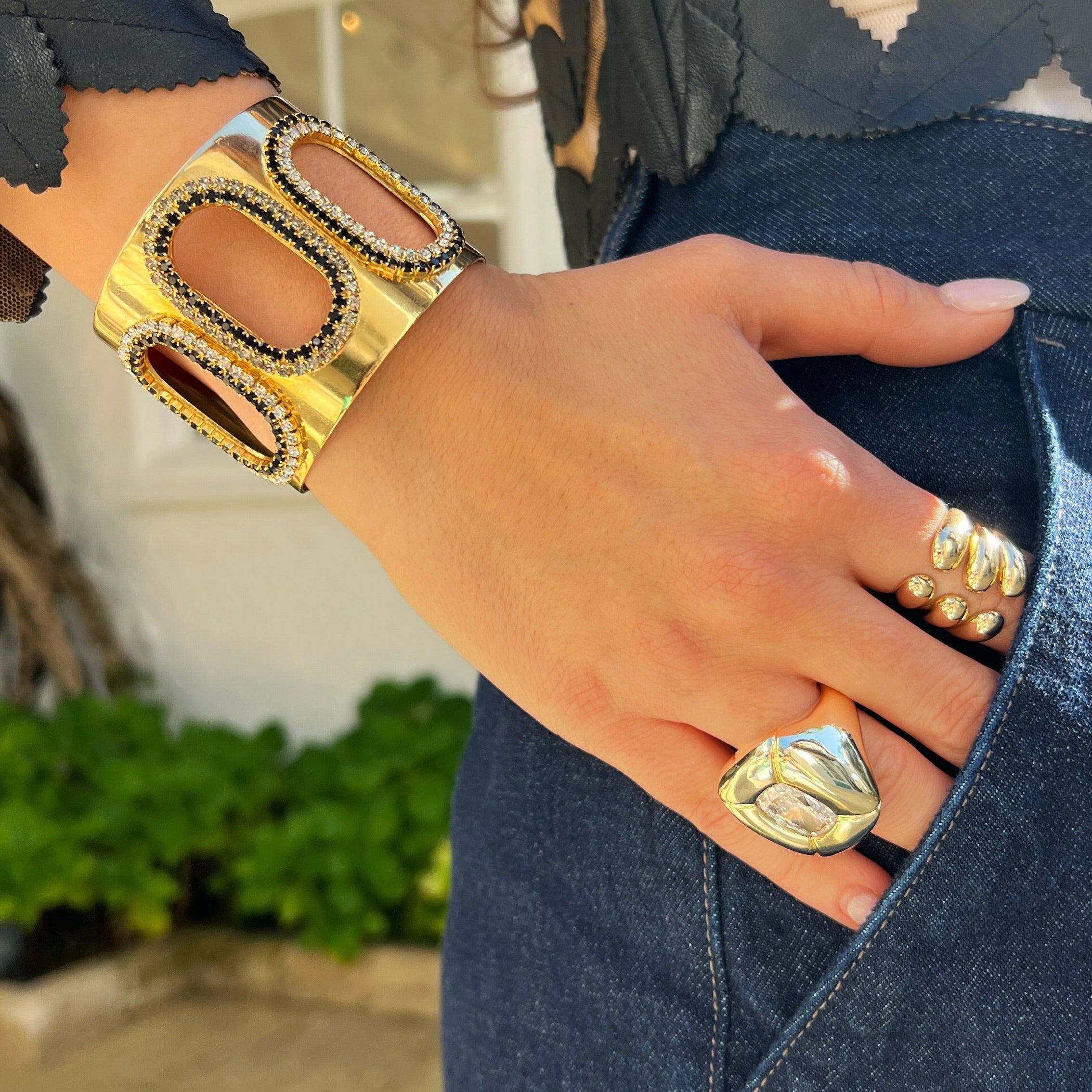 Close-up of a person wearing gold bracelets and rings with a blurred outdoor background