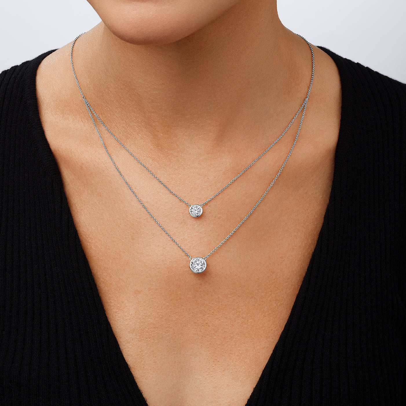 Two silver necklaces with round pendants on a person wearing a black top.
Double Bezel Solitaire Chain Necklace
White Gold Plated
Small Bezel: 1.5 Carat
Large Bezel: 3.0 Carat
16-20" Long
Faux Bezel Diamond