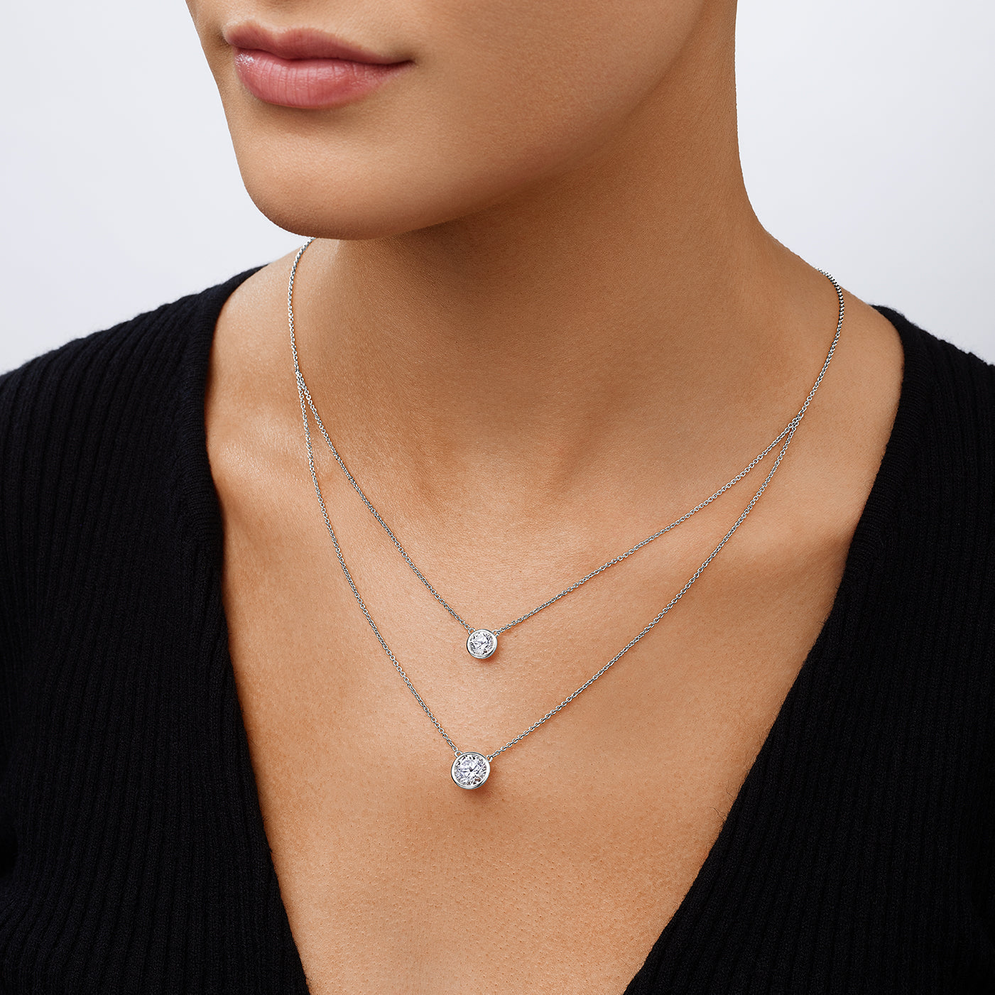 Close-up of a person wearing two silver necklaces with round pendants on a plain background
Double Bezel Solitaire Chain Necklace
White Gold Plated
Small Bezel: 1.5 Carat
Large Bezel: 3.0 Carat
16-20" Long
Faux Bezel Diamond