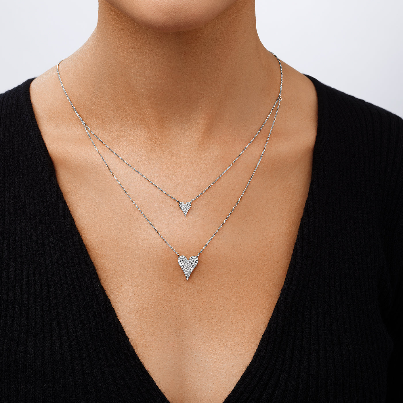 Two heart-shaped silver necklaces on a person wearing a black top.
Layered Double Heart Necklace
White Gold Plated
Small Heart: 0.38" Long X 0.38" Wide
Large Heart: 0.50" Long X 0.63" Wide
16-20" Long
Faux Pave Diamond