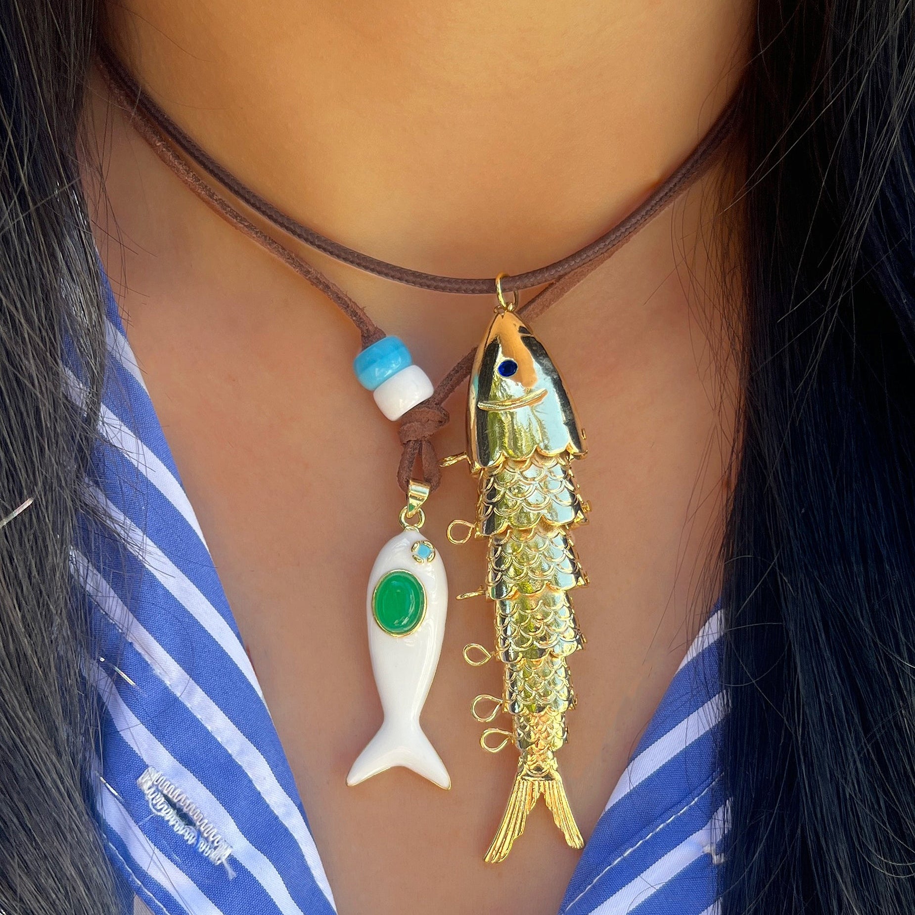 Necklace with two fish pendants on a person wearing a blue and white striped shirt.