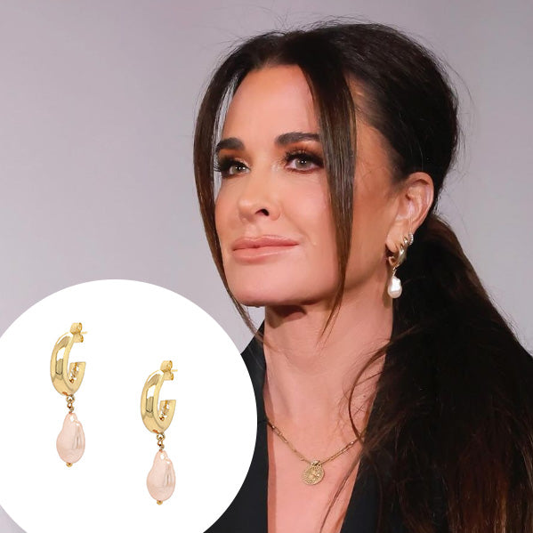 These exquisite hoops feature a stunning light pink pearl elegantly set in your choice of yellow or white gold plating, embodying the essence of elegance and hope. These gorgeous earrings perfectly complement any ensemble, making them a versatile addition to your jewelry collection.  Pink Pearl Drop on Small Hoop Pieced Earrings  Yellow or White Gold Plating Faux Light Pink Pearl 1.75" Long X 0.42" Wide As worn by Kyle Richards.