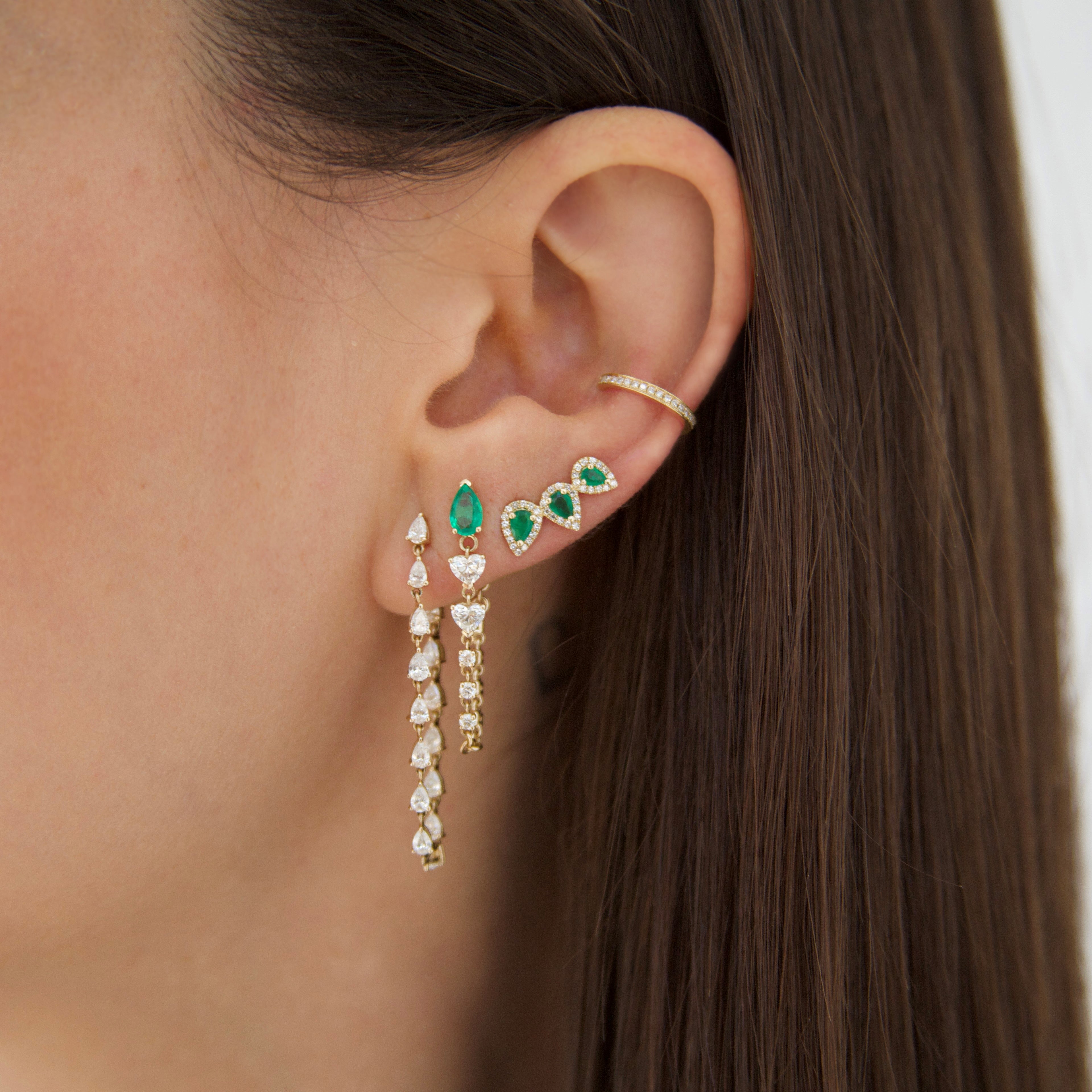 Diamond teardrop earring on woman's ear with emerald earrings and diamond ear cuff