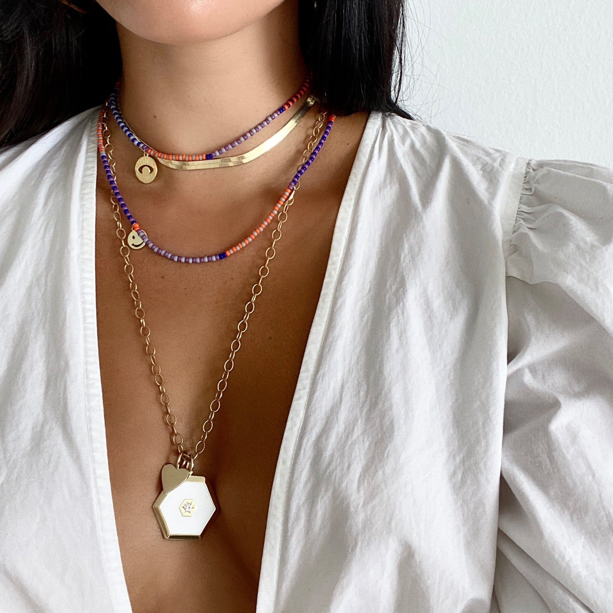 Heart pendant charm worn with white enamel hexagon charm on yellow gold chain necklace