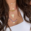 Woman wearing pave love necklace above layered yellow gold and rainbow chain link necklaces