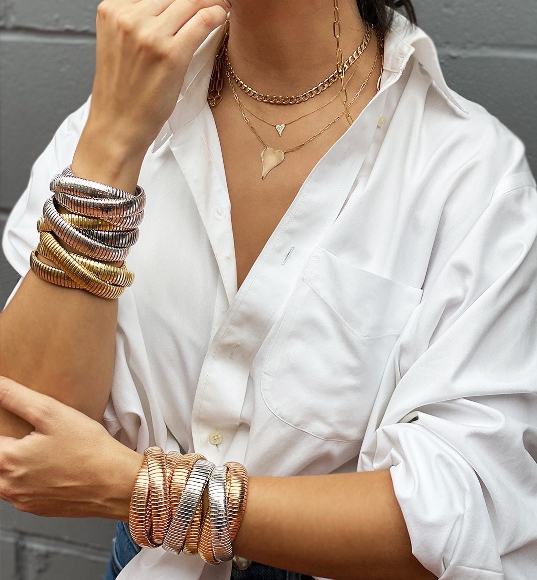 Diamond small heart necklace worn with layered gold chains and paired with classic triple strand bracelets