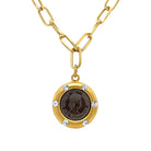 Gold necklace with a round coin pendant featuring a coin and small crystals on a white background
