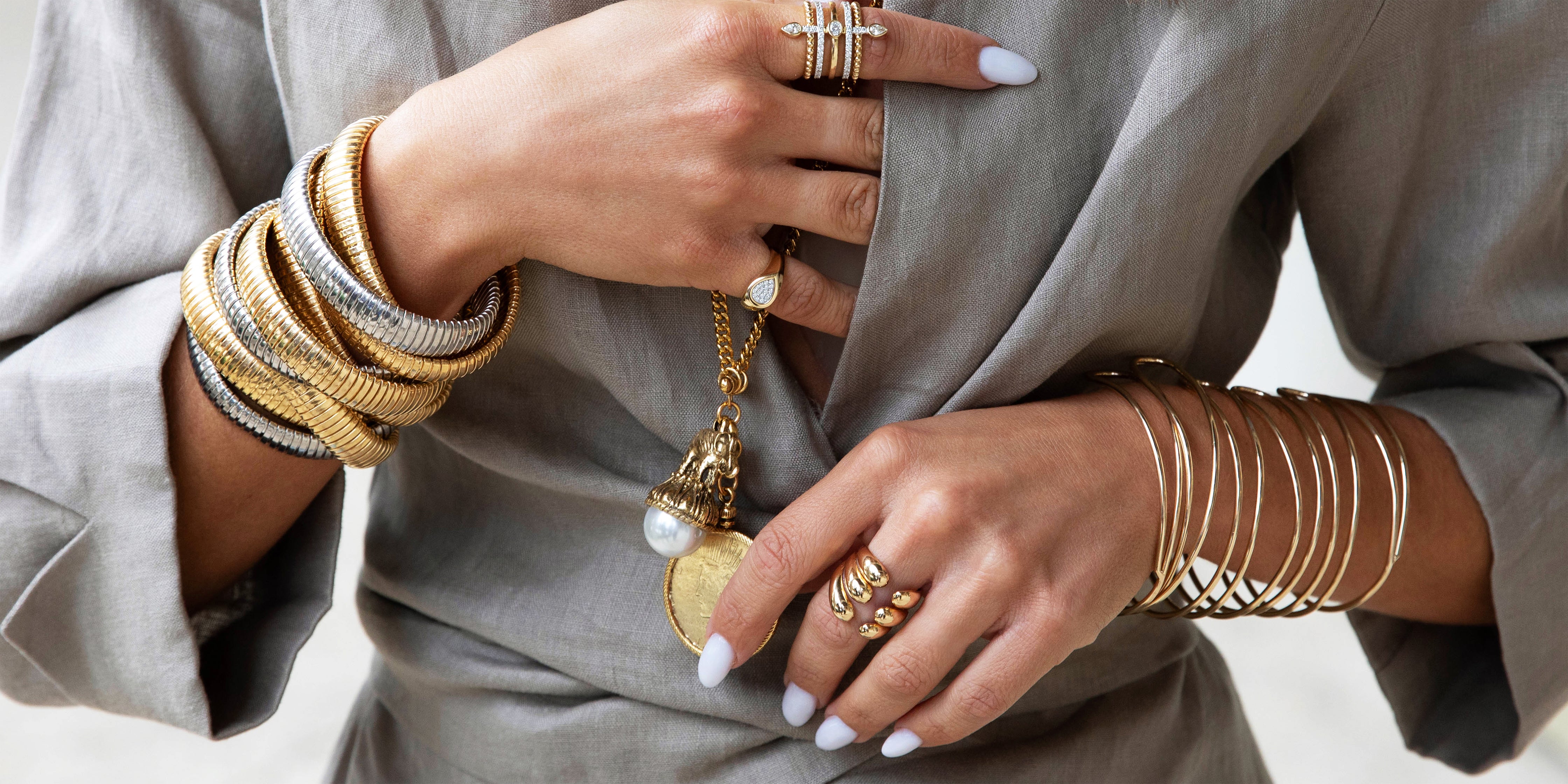 Close-up of hands wearing gold jewelry on a neutral background