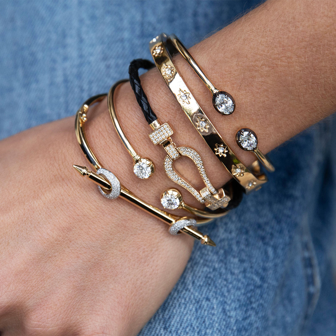 Close-up of a wrist wearing multiple gold with gemstones against a blue denim background.