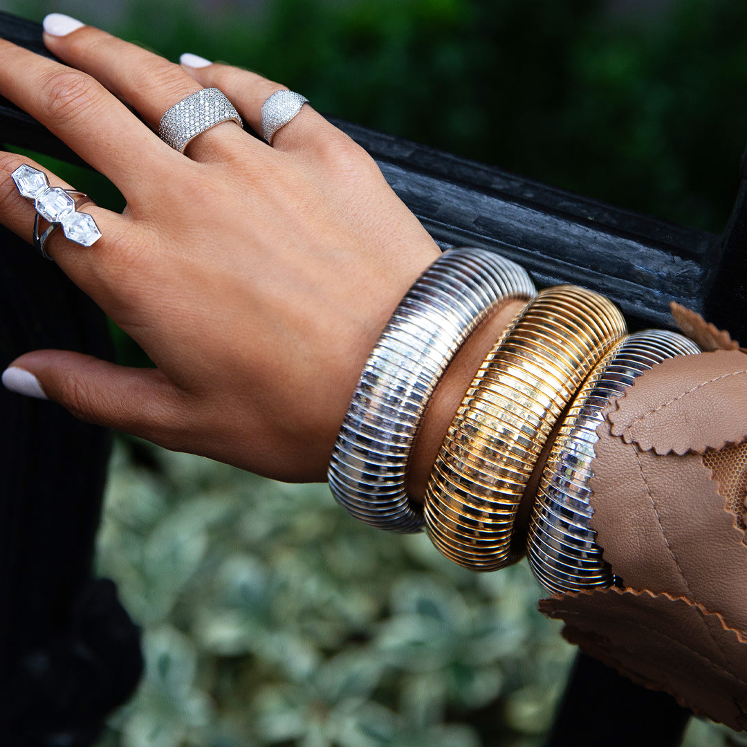 Hand wearing multiple silver and gold bracelets with rings on a blurred background