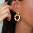 Close-up of a person wearing a gold earring with pink pearls.
