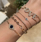 Diamond + sapphire evil eye bracelet displayed with yellow gold and pave bracelets on wrist