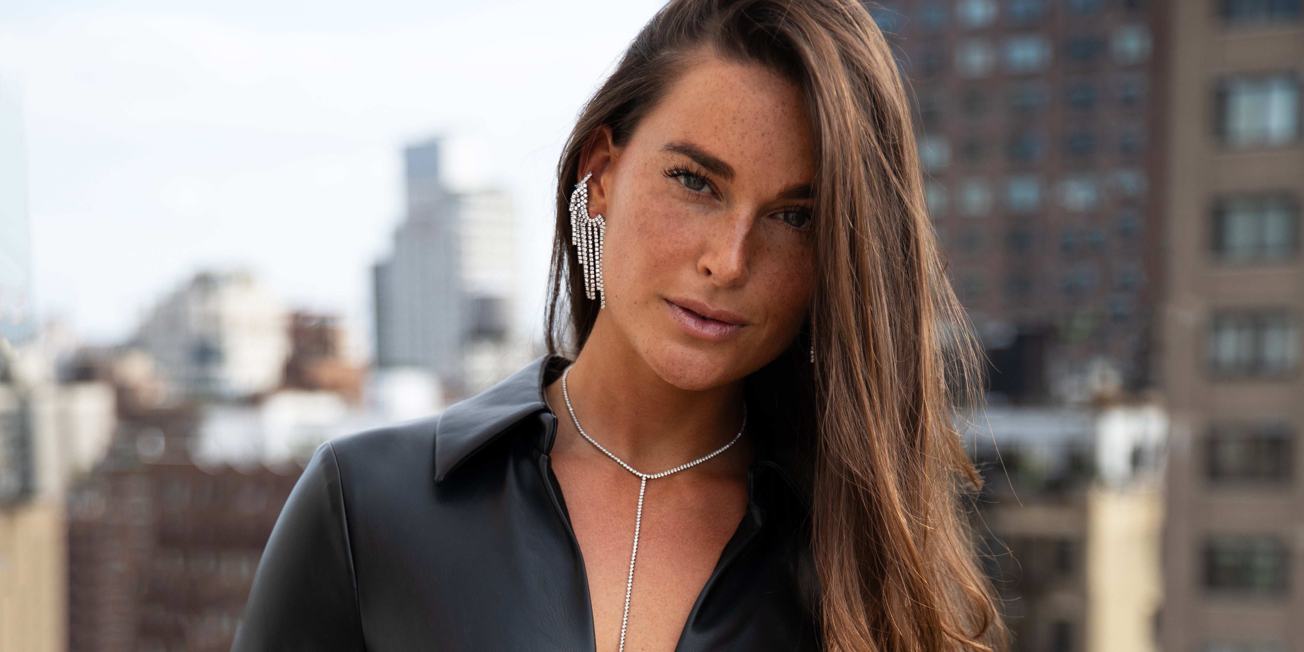 Woman with long hair and earrings standing in front of a cityscape