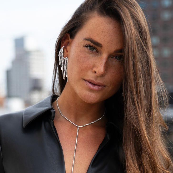 Woman with long hair and earrings standing in front of a cityscape