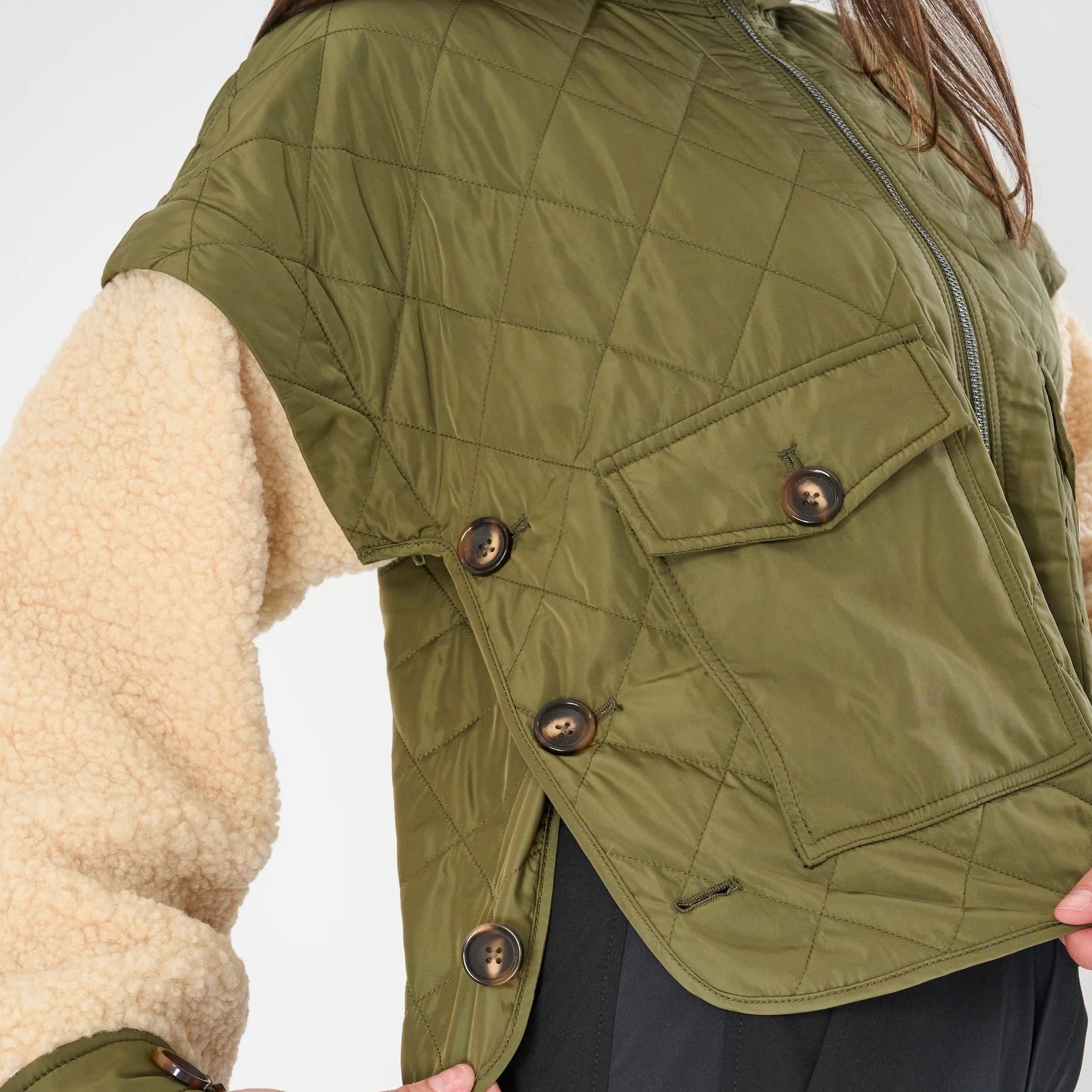 Green quilted jacket with beige lining worn by a person on a white background
