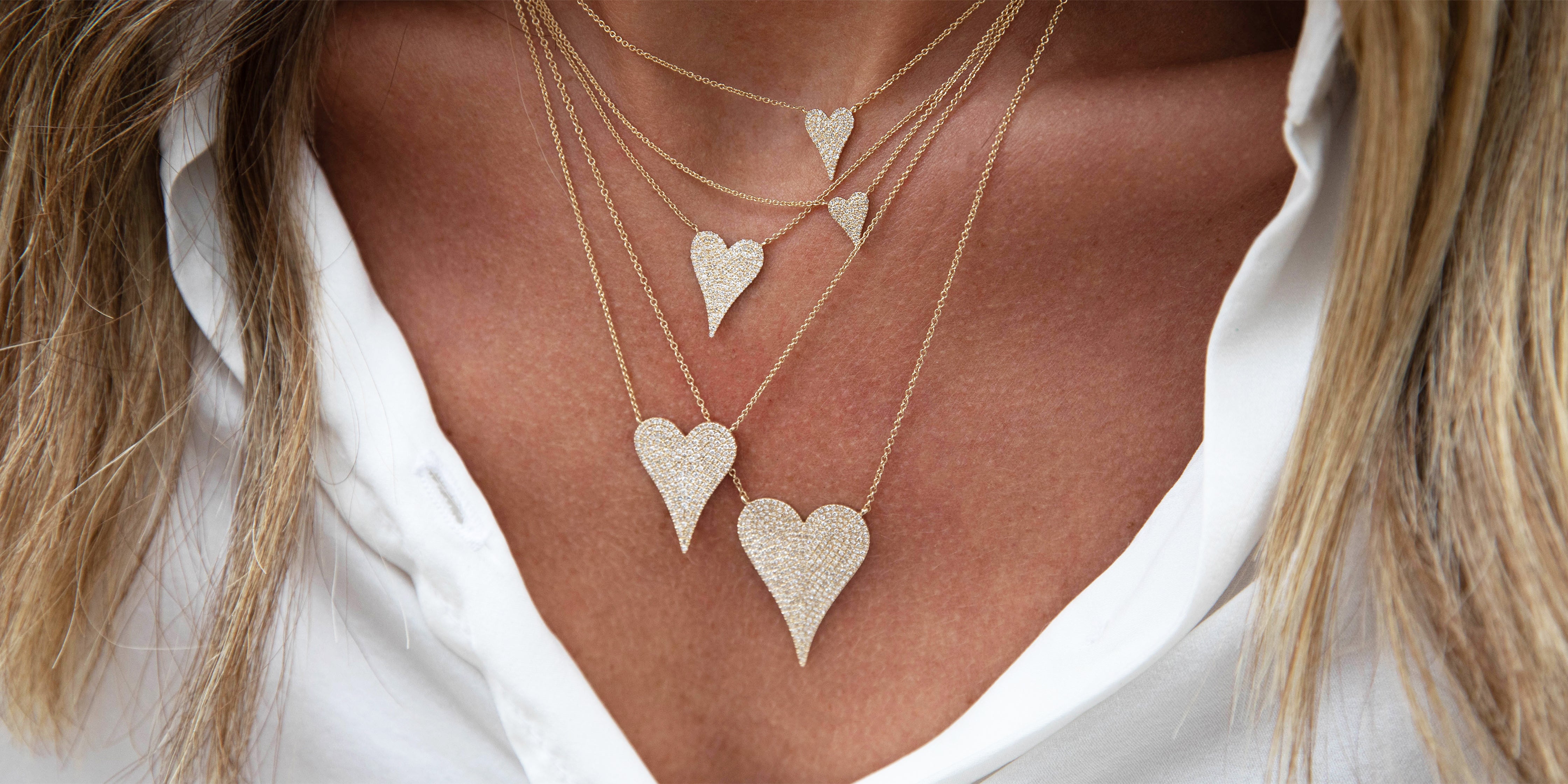 Close-up of a person wearing multiple gold heart-shaped necklaces on a white shirt.