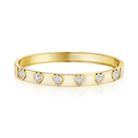 A polished yellow gold bangle bracelet featuring five small heart-shaped clear gemstones set along the front, displayed on a clean white background with a soft reflection.