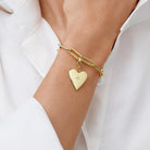 Gold bracelet with a heart-shaped charm on a person's wrist against a white background