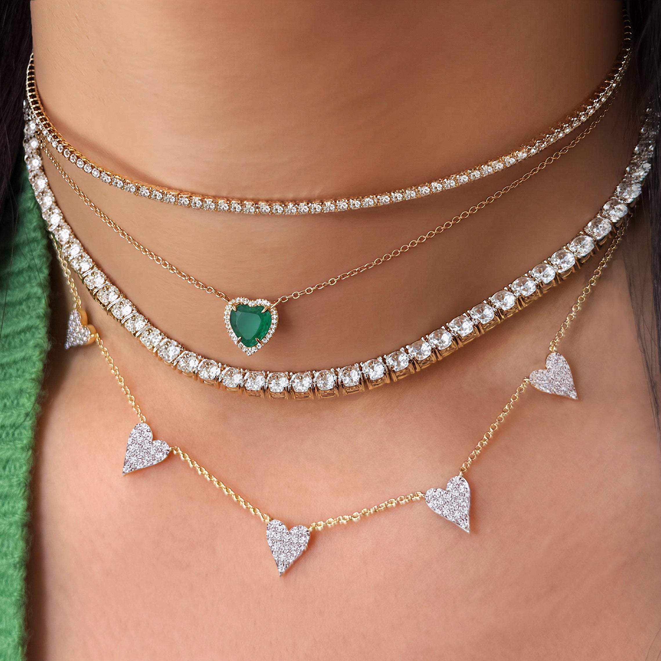Close-up of layered necklaces with heart pendants on a person wearing a green and yellow garment.