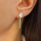 Close-up of a woman's ear wearing a gold teardrop earring with a central gemstone and dangling chain.