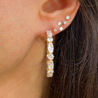 Close-up of an ear wearing gold hoop earrings with clear gemstones.