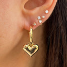 Close-up of an ear wearing gold heart-shaped hoop earrings with small diamond stud earrings.
