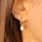 Close-up of an ear wearing gold hoop earrings with pearl drops and silver stud earrings.