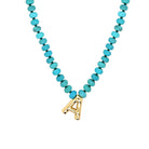 Necklace with turquoise beads and a gold letter 'A' pendant on a white background