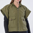 Woman wearing a green vest over a black long-sleeve shirt on a white background