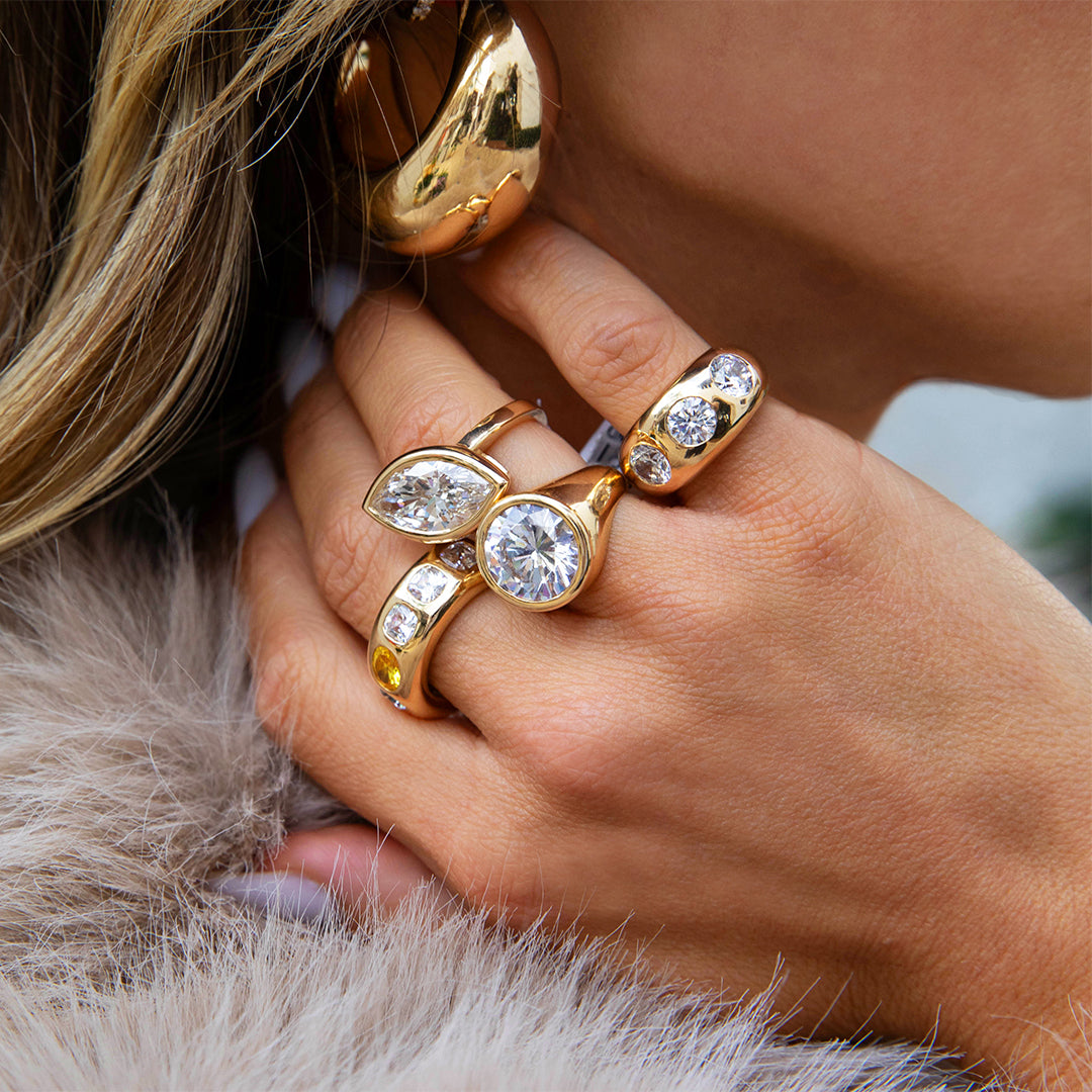 Close-up of a hand wearing gold rings with gemstones, holding a fur coat.