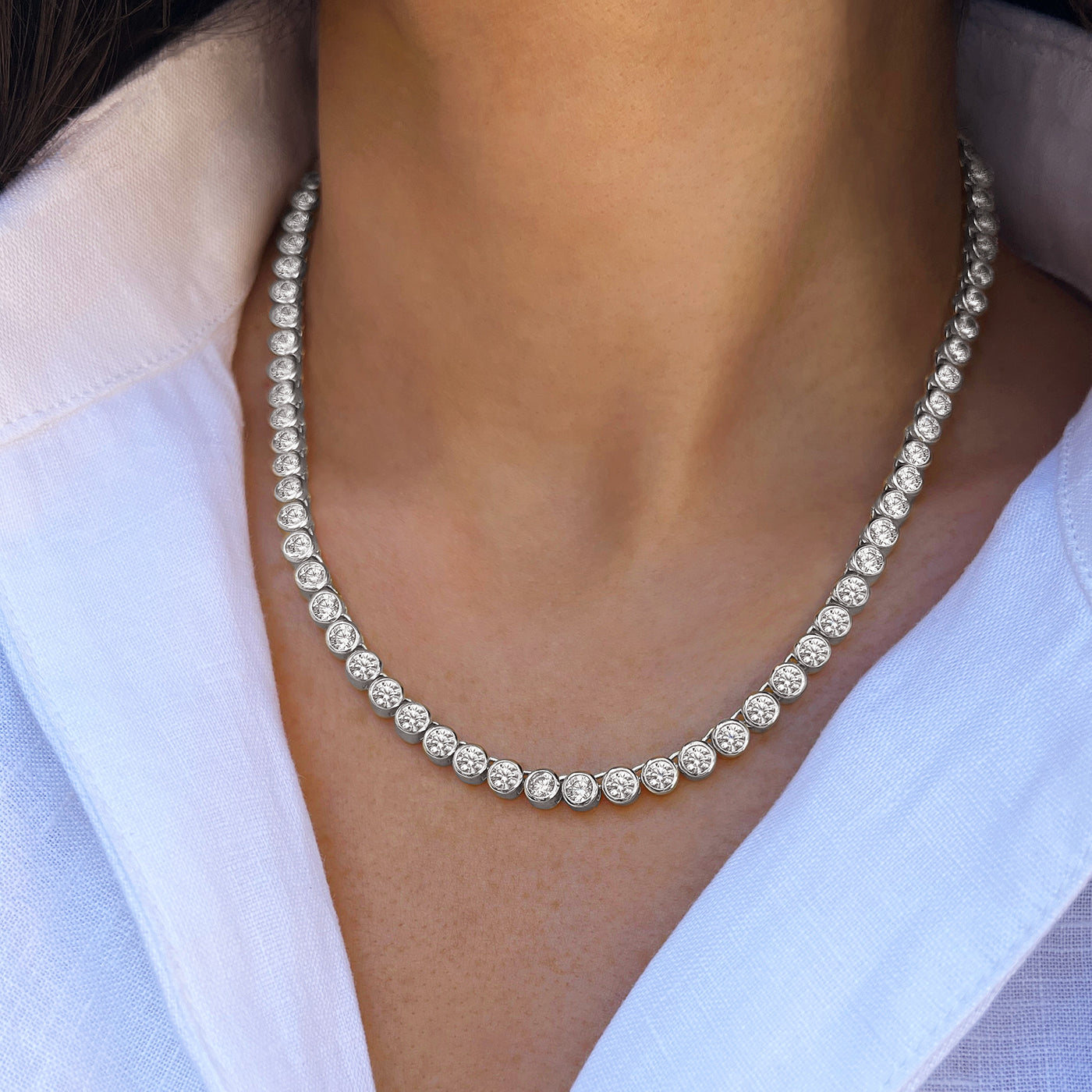 A close-up of a model wearing a silver tennis necklace with round-cut clear stones, styled with a white collared shirt.