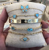 Turquoise & diamond butterfly bracelet on display pillow with other yellow gold & turquoise bracelets