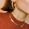 Woman wearing wide yellow gold hoop earrings with safety pin gold chain
