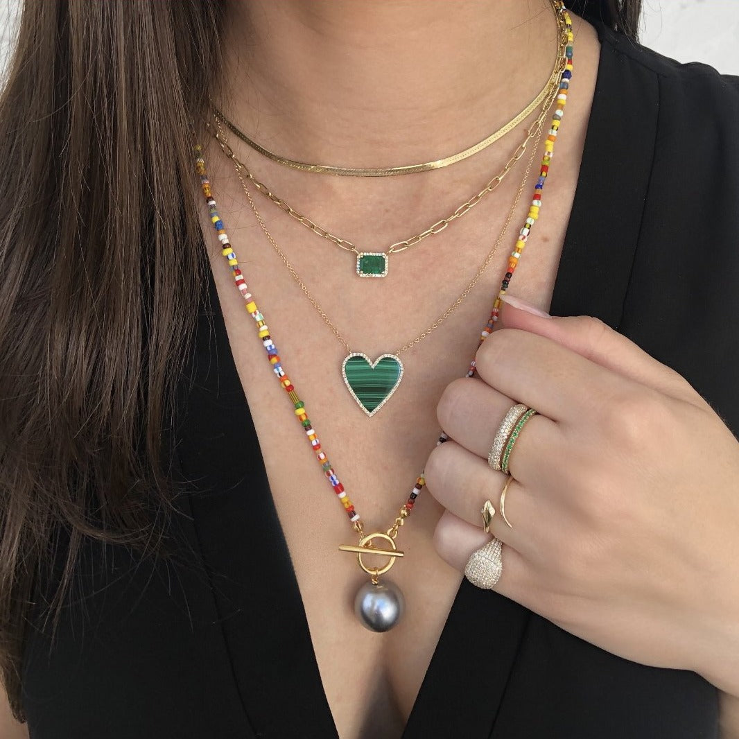 Woman wearing herringbone necklace layered with yellow gold chain link and toggle necklaces
