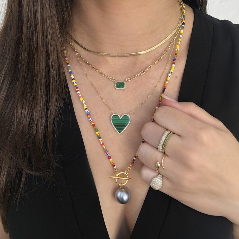 Malachite heart necklace worn layered with yellow gold chains and rainbow beaded necklaces