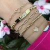 Yellow gold, diamond heart chain bracelets and beaded bracelet on a wrist.