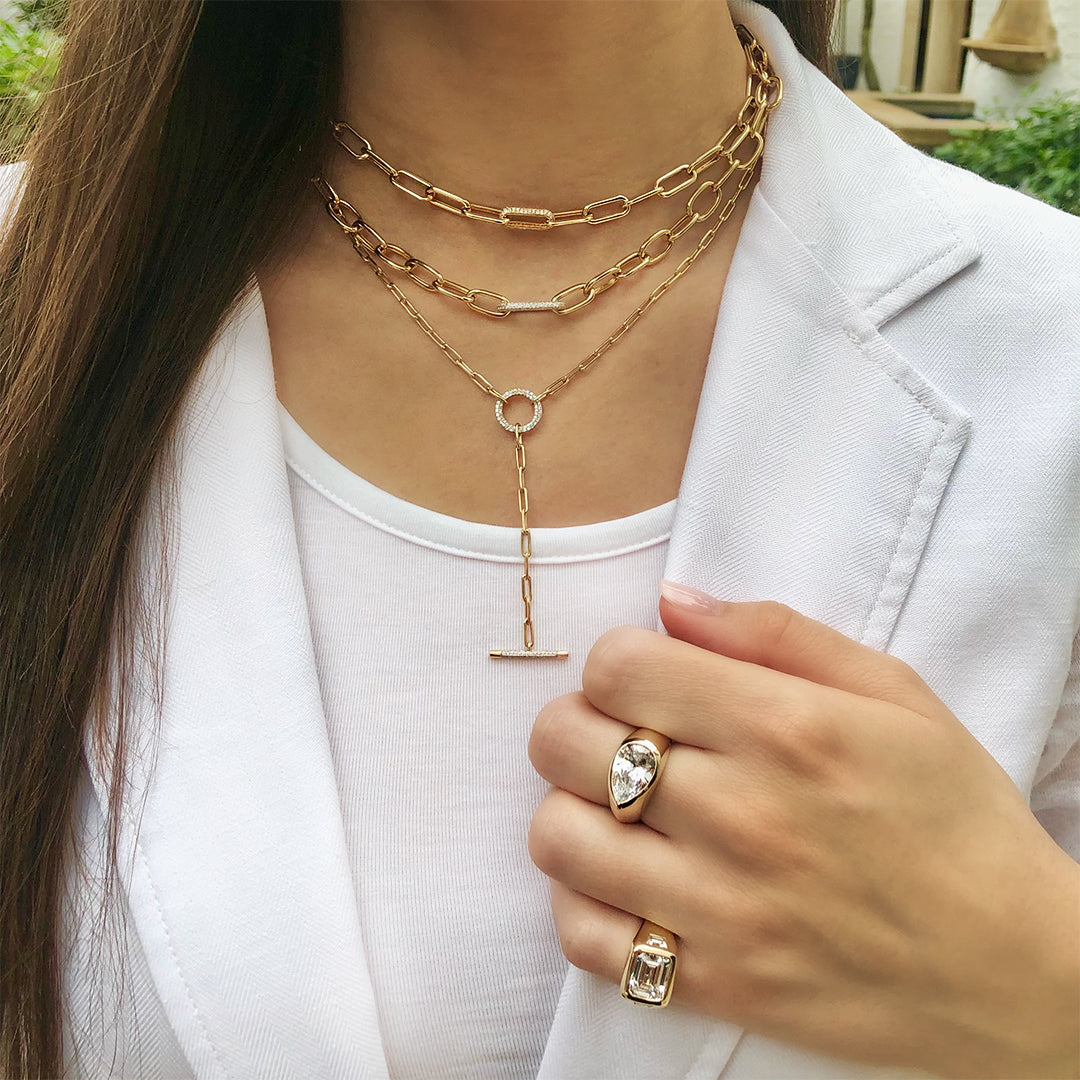 Woman wearing pear shape ring with another gypsy ring and yellow gold chain link necklaces from collection