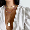 White enamel hexagon charm pendant worn on long gold chain and layered with rainbow beaded choker charm necklaces
