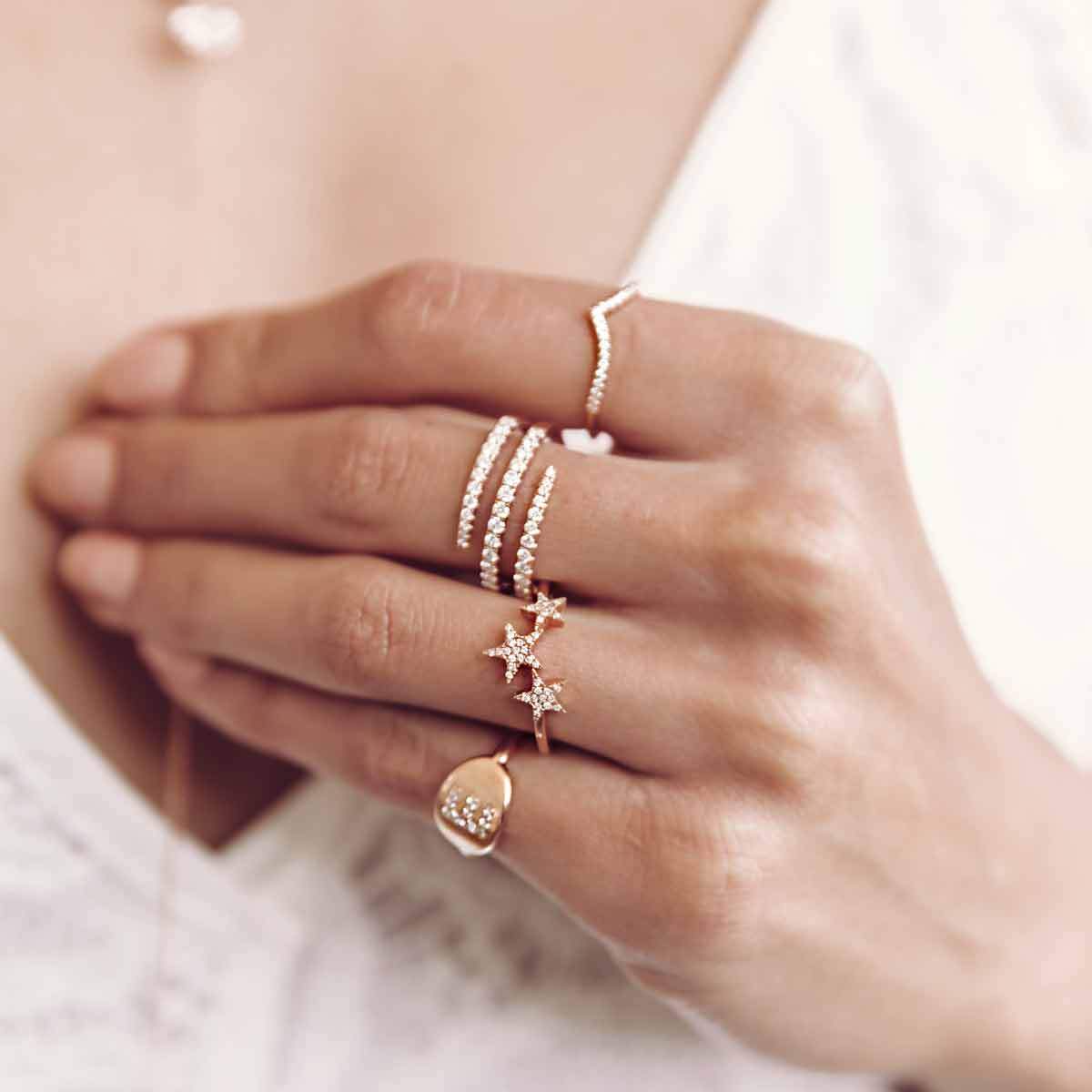 diamond coil ring on woman's hand with initial signet, pave star and diamond pave rings