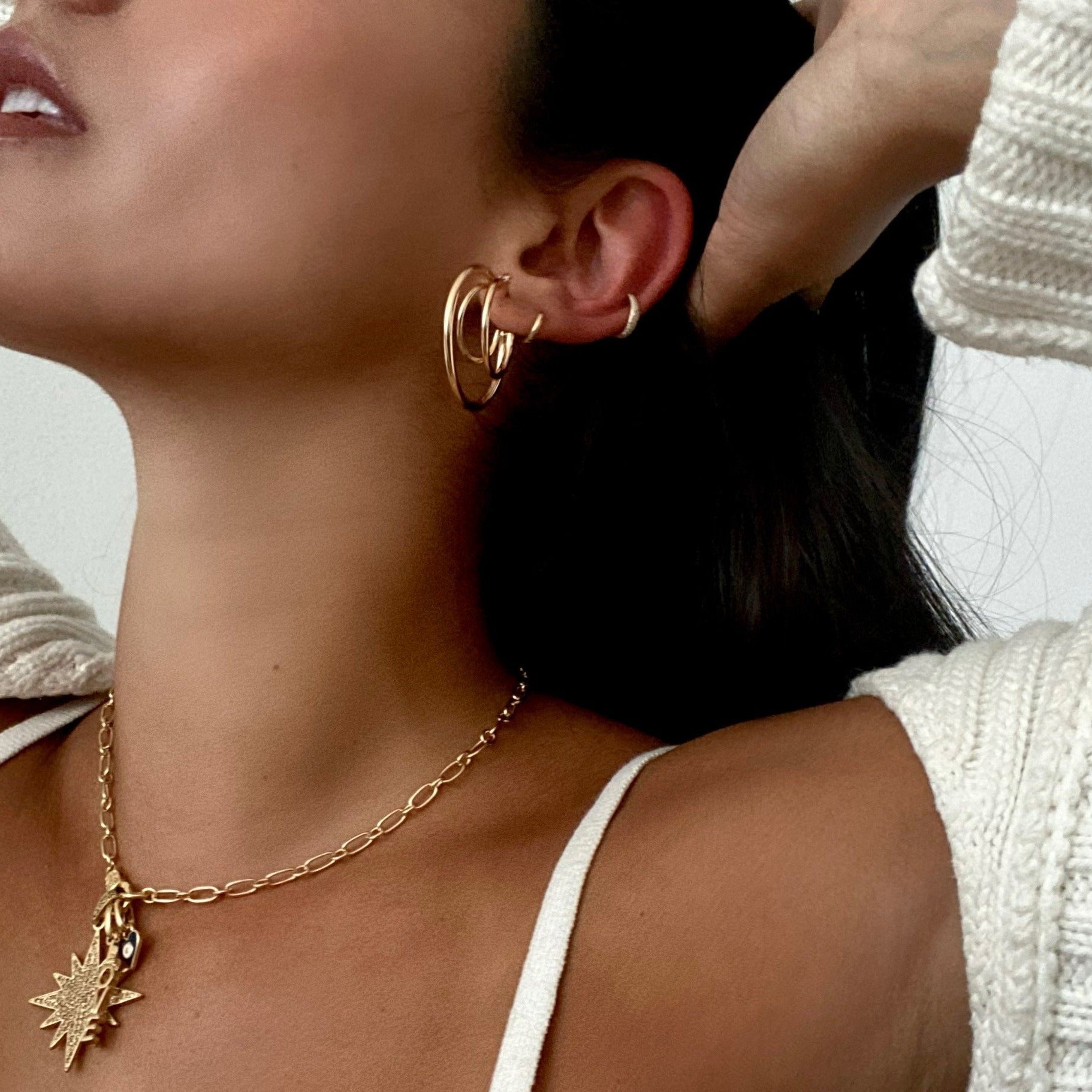 Woman wearing gold huggies with triple hoops and yellow gold chain link charm necklace