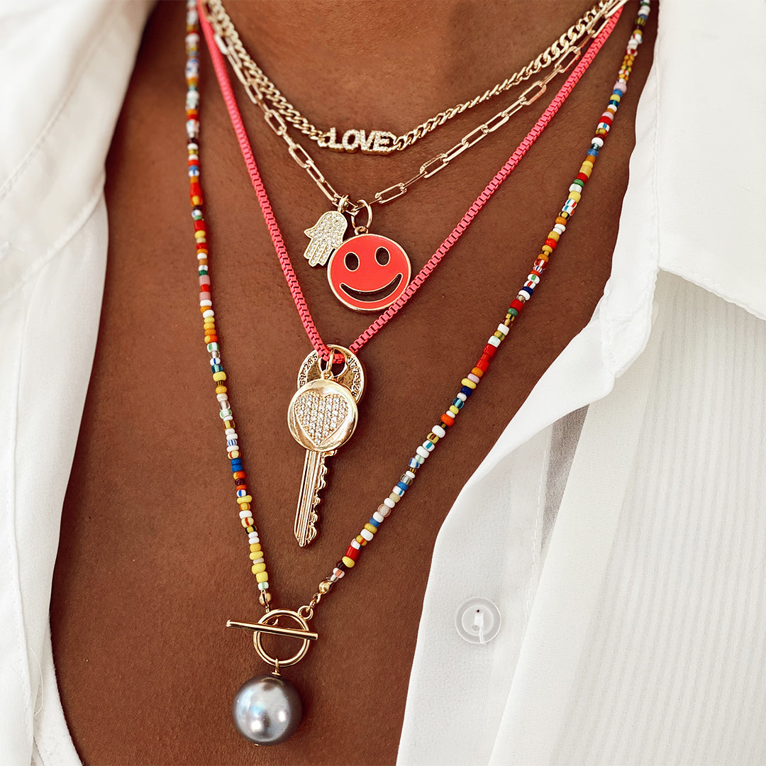 Woman wearing pave love necklace above layered yellow gold and rainbow chain link necklaces