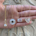 Diamond & pearl heart necklace paired with yellow gold statement necklaces on a sandy background