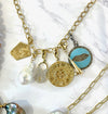 Charm necklace chain with yellow gold, turquoise, and pearl pendants, against a white marbled background