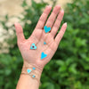 Turquoise & diamond heart necklace displayed on woman's palm with other turquoise heart necklaces and bracelets in different sizes