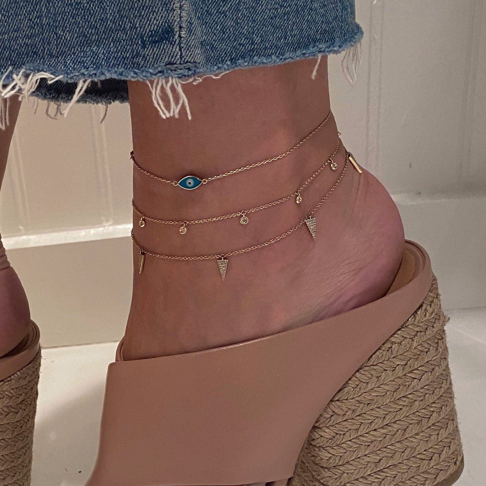 Diamond dangle anklet worn layered with others in yellow gold